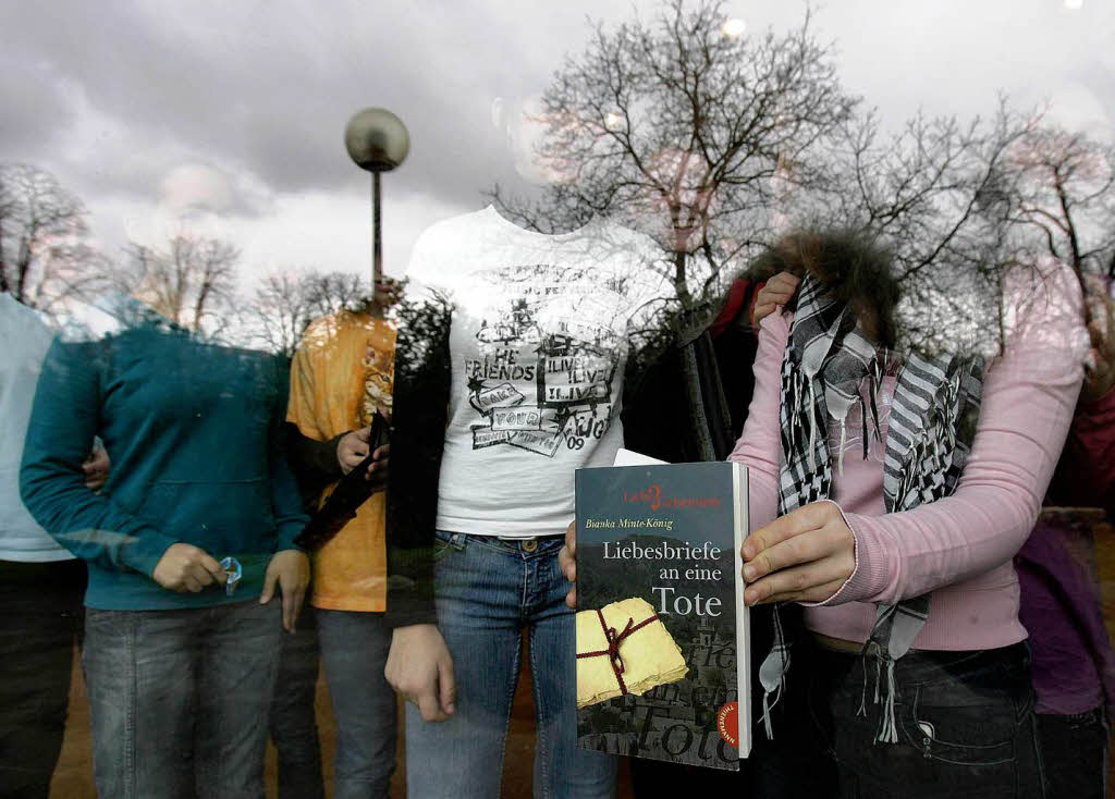 Eine Schlerin hlt ein Buch mit dem Titel „Liebesbriefe an eine Tote“ an eine Scheibe.