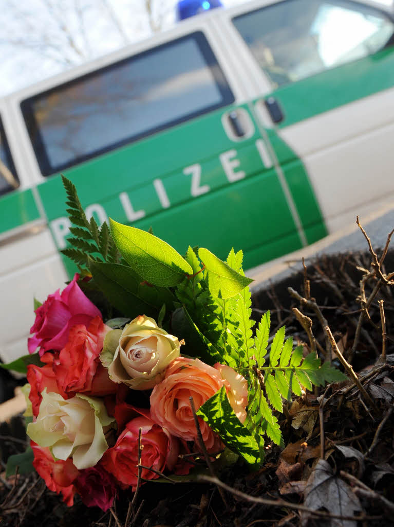 Ein Polizeifahrzeug fhrt an einem Blumenstrau vorbei, den Passanten an der Strae abgelegt haben.