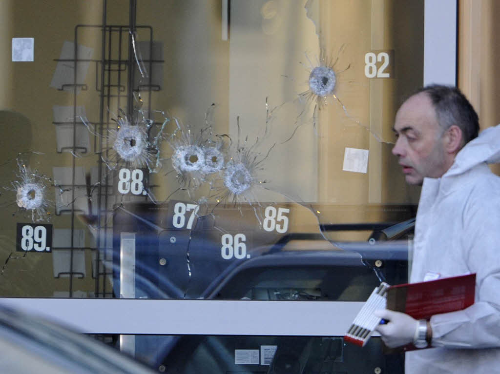 Ein Beamter der Spurensicherung vor einer zerschossenen Scheibe des Autohauses, an dem der Amoklauf endete.