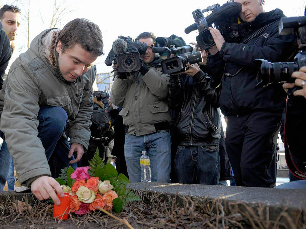 Ein junger Mann legt einen Blumenstrau an der Schule nieder.