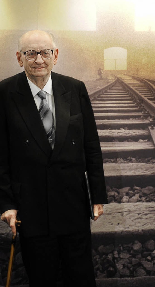 Bartoszewski steht vor einem Bild des Lagers Auschwitz.   | Foto: DPA