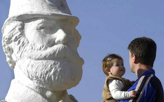 Vater und Kind vor einer Skulptur, die Adem Jashari zeigt.   | Foto: DPA