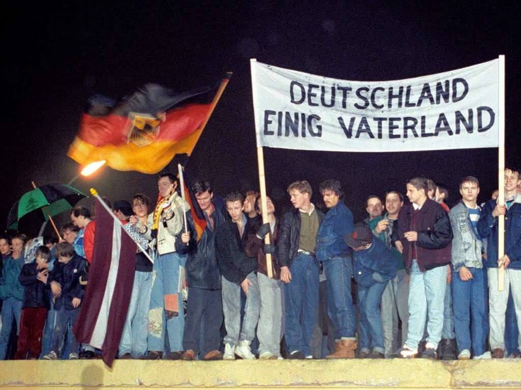 Mit der Deutschlandfahne und einem Transparent "Deutschland Einig Vaterland" stehen zahlreiche Berliner am 22.12.1989 auf der Berliner Mauer am Brandenburger Tor. In Osteuropa begann ein Erosionsprozess, der am 9. November 1989 mit dem Fall der Mauer einen Hhepunkt erreichte und eine vllig neue Weltordnung einleitete.