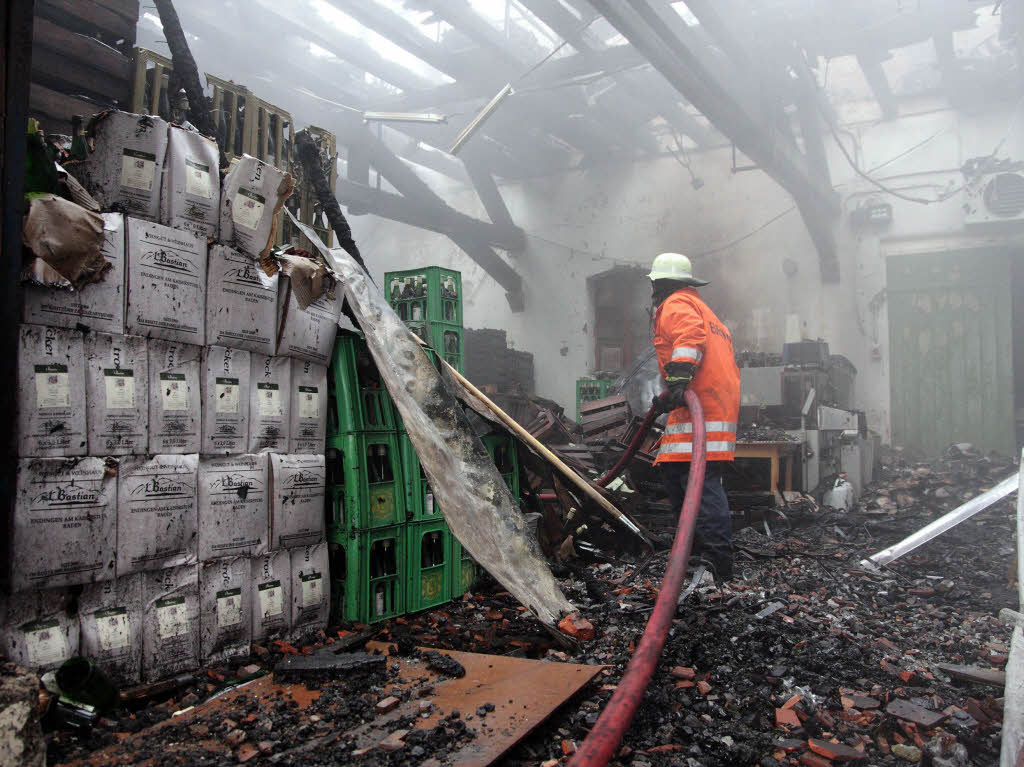 Ein Feuerwehrmann inmitten verbrannter und aufgeweichter Kartons sowie von der Hitze deformierter und geschmolzener Weinkisten bei Nachlscharbeiten.