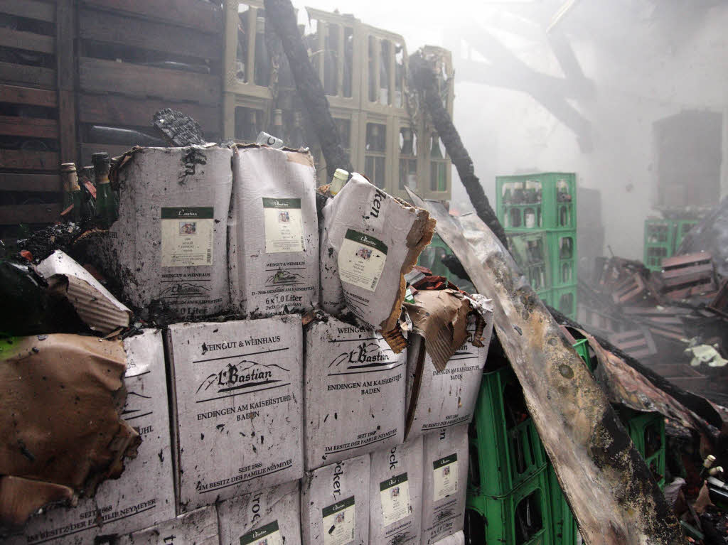 Verbrannte und aufgeweichte Kartons und von der Hitze deformierte und geschmolzene Weinkisten im vllig zerstrten Lagergebude