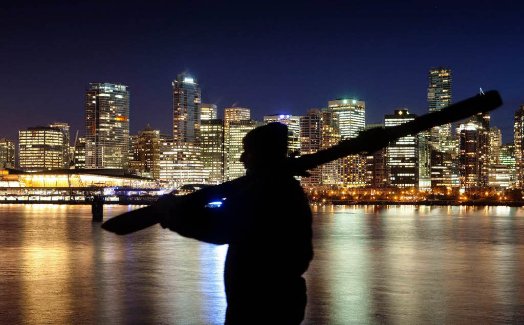 Ein Mann trgt ein Paar Skier. Im Hintergrund die nchtlichen Skyline von Downtown Vancouver