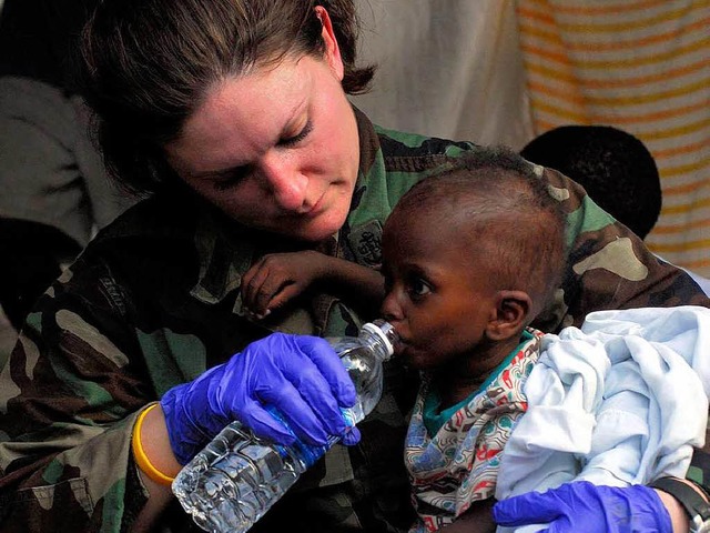 Ein dehydriertes Kind bekommt Wasser von einer Soldatin.  | Foto: ddp