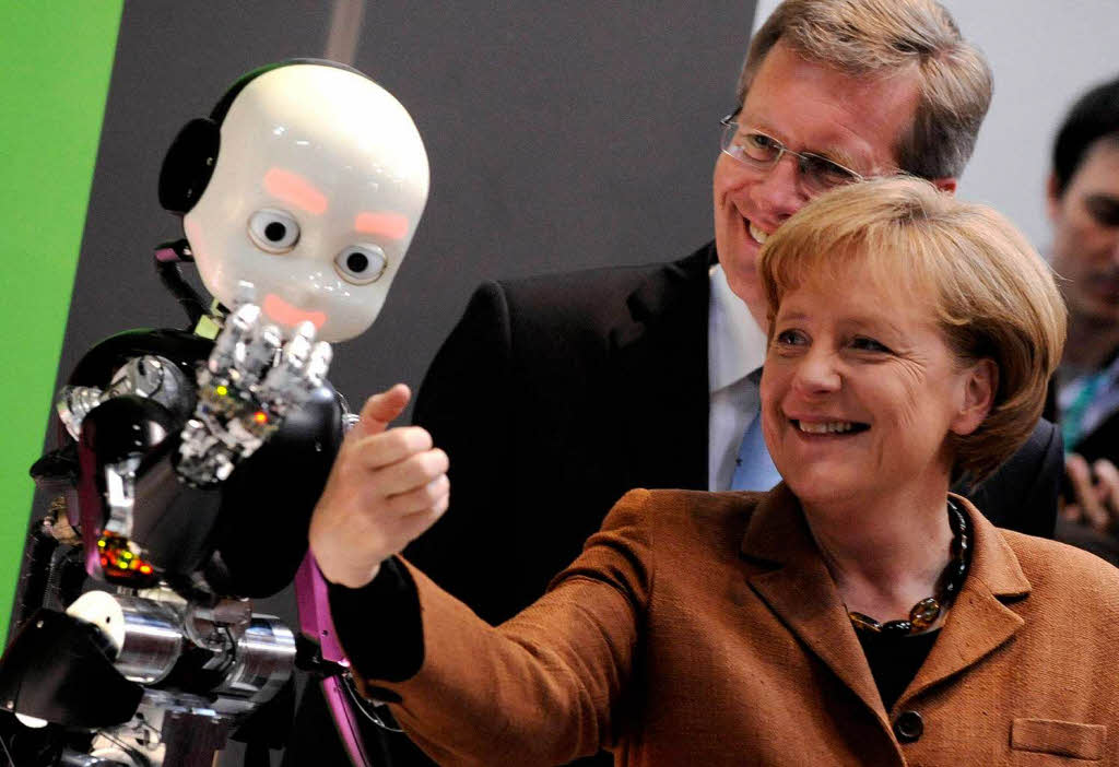 Angela Merkel  schauen sich  am italienischen Gemeinschaftsstand den "Robot iCub" an.