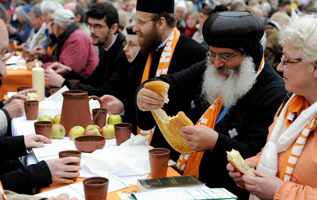 Besucher teilen am Freitag  am Odeonsplatz bei einer orthodoxen Vesper an einem gedeckten Tisch das Brot miteinander.