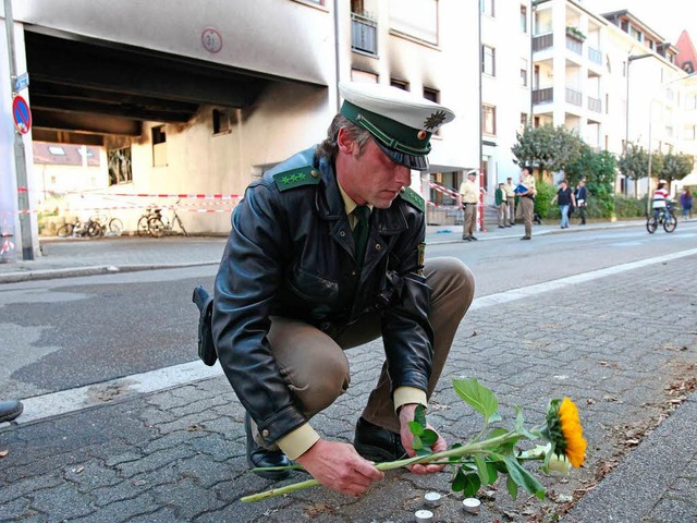 Ein Polizist legt in Lrrach am Tatort eine Blume nieder   | Foto: dpa