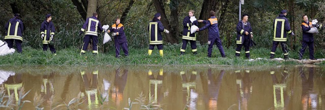 Feuerwehrleute sichern am Mittwochnach...en durchweichten Deich mit Sandscken.  | Foto: dpa