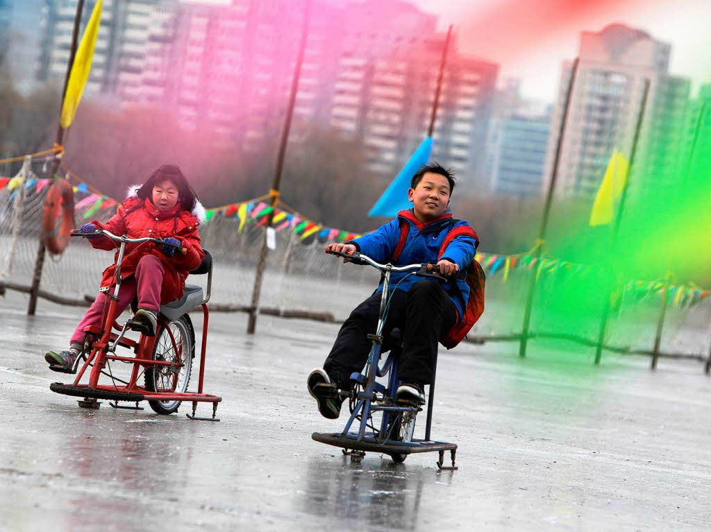 Chinesische Kinder fahren mit Eisrdern ber einen gefrorenen See bei Peking.