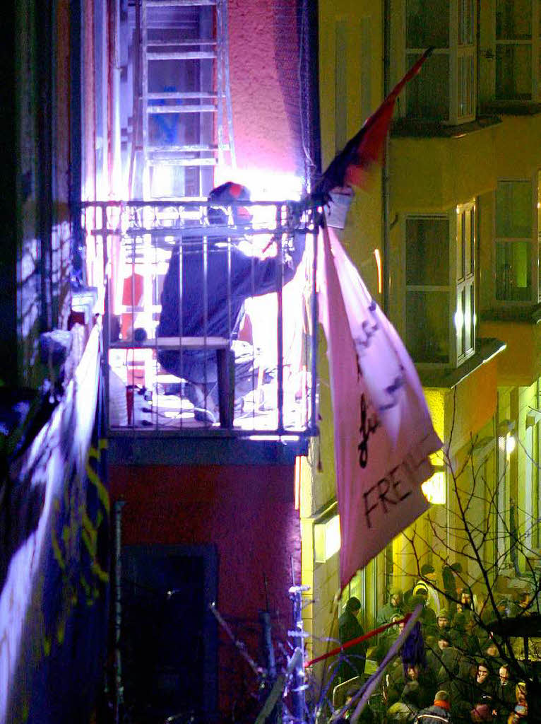Ein vermummter Hausbesetzer schweit auf einem Balkon am besetzten Haus Barrikaden zusammen.