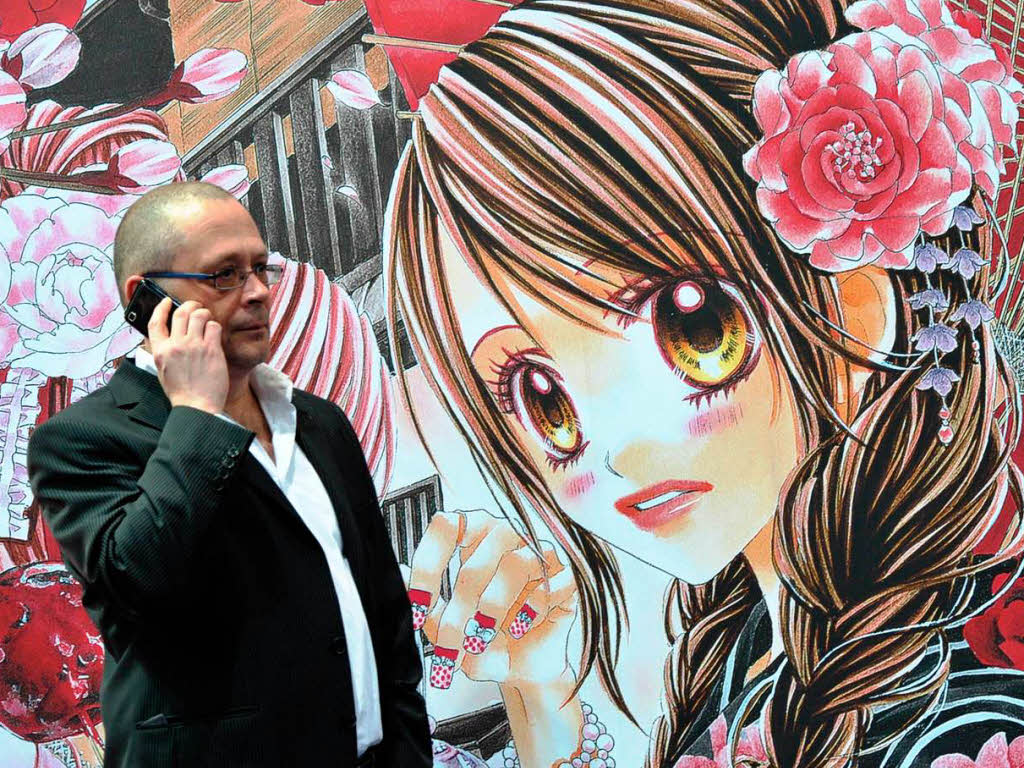 Ein Mann telefoniert vor einem Aufsteller mit einer Manga-Figur auf der Buchmesse.
