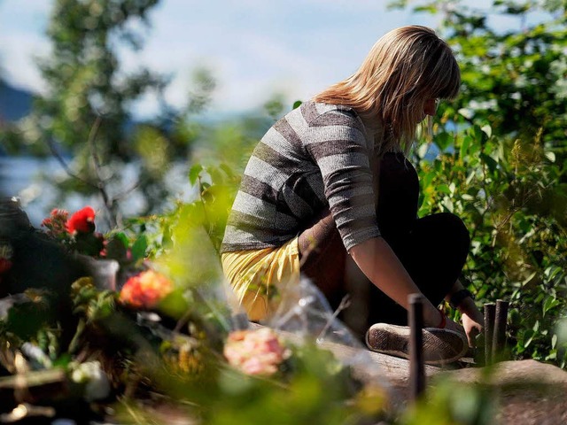 Eine berlebende des Massakers sitzt a...Fjordinsel Utya, an der Blumen liegen  | Foto: dpa