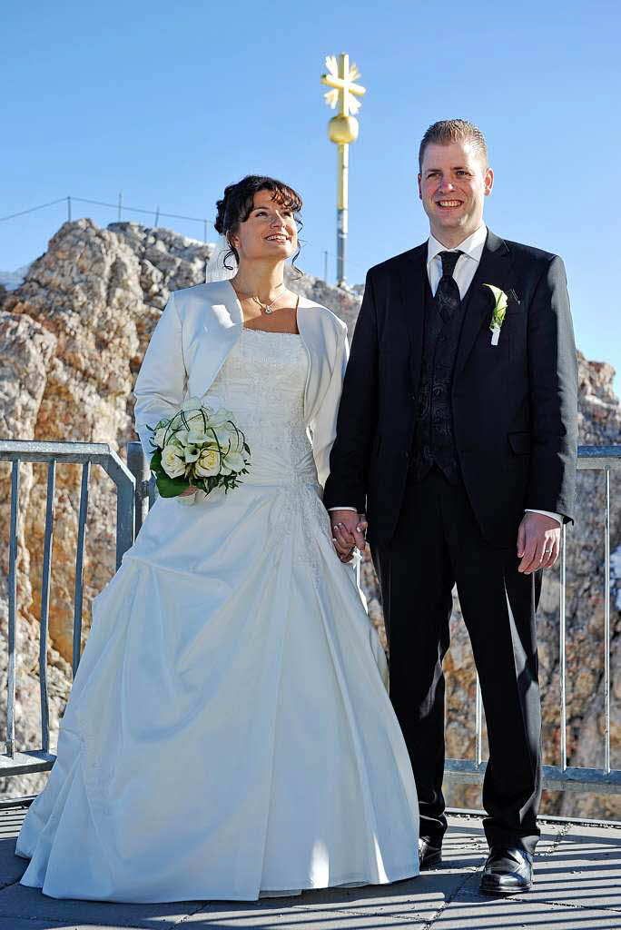 Graziella und Michel Kristahn posieren  vor dem Gipfelkreuz der 2962 Meter hohen Zugspitze.