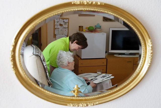 Eine Betreuerin schaut sich zusammen mit einer Frau ein Fotoalbum an.   | Foto: DPA