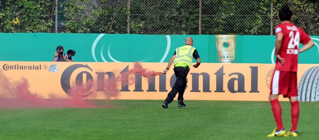 Ein Ordner entfernt die Pyrotechnik vom Spielfeld.   | Foto: dpa