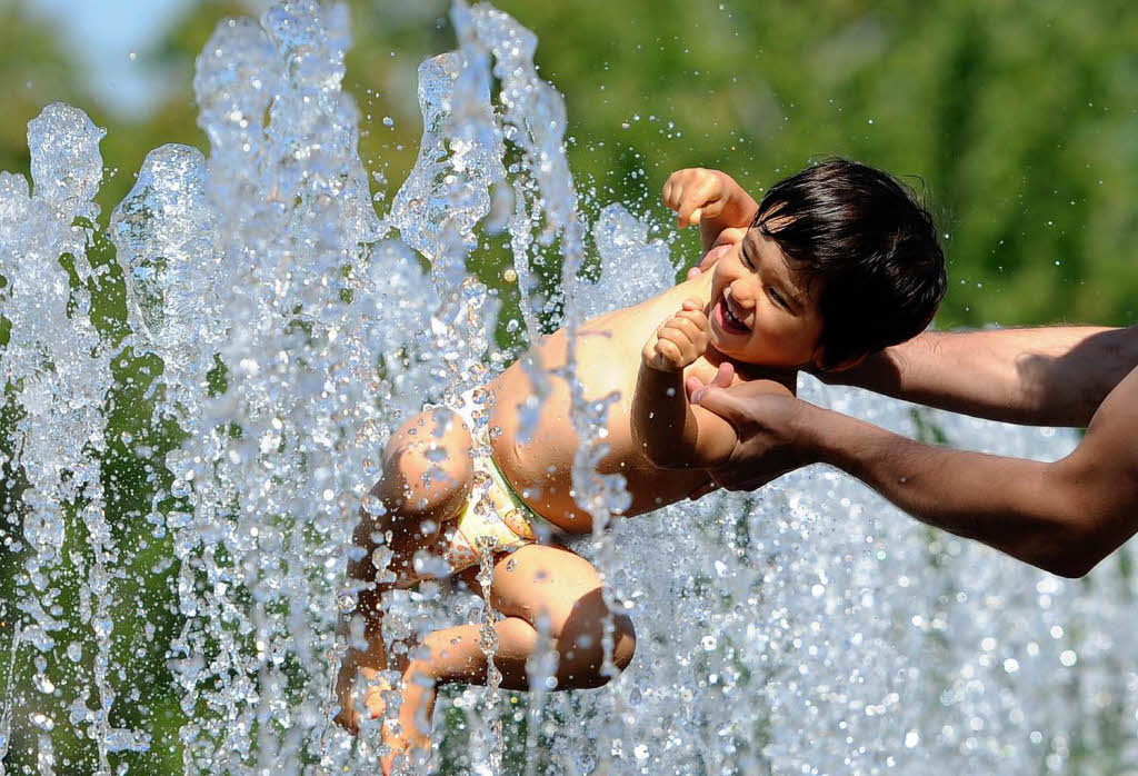 In der Hauptstadt hlt eine Mutter ihr Kind in die Wasserfontnen eines Springbrunnens.