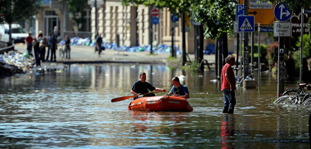 Feuerwehrleute fahren mit einem Schlauchboot durch das Hochwasser der Saale auf dem Robert-Franz-Ring in Halle