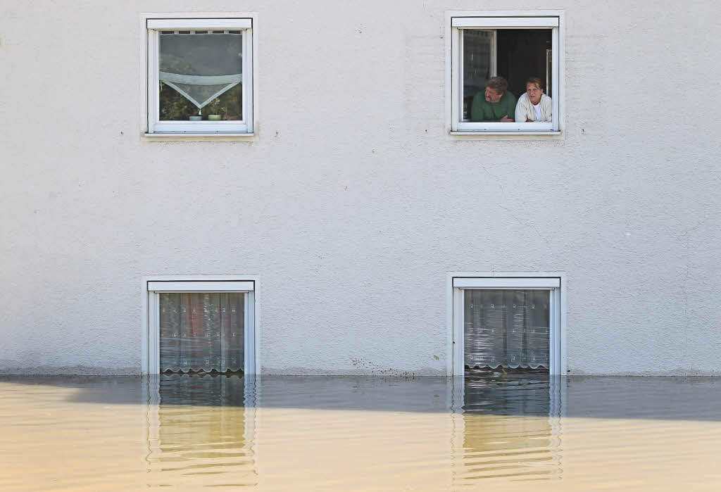 Bewohner eines vom Hochwasser eingeschlossenen Hauses schauen in Deggendorf (Bayern) aus dem Fenster.