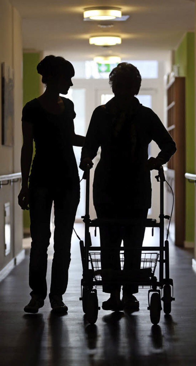 Eine Pflegerin begleitet eine Frau mit...ch die Gnge eines Altenheims in Kln.  | Foto: dpa