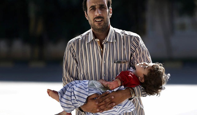 Ein Syrer trgt sein verletztes Kind ber die Grenze in die Trkei.   | Foto: DPA