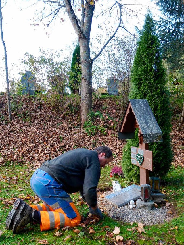 Andr Cox reinigt  das Holzkreuz, auf ... Sterbedaten vermerkt sind, von Laub.   | Foto: Peter Stellmach