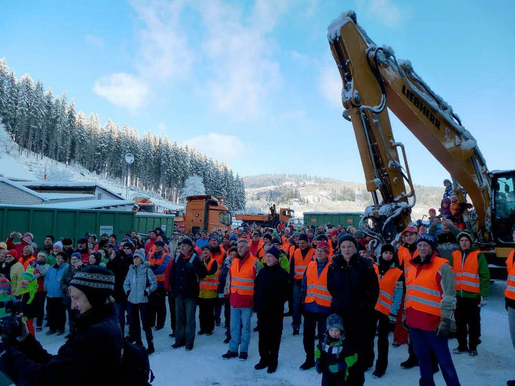 Die Zuschauer verfolgen das Geschehen. Der Bagger, der den  Schneehaufen  „anbeien“ wird, steht schon parat.