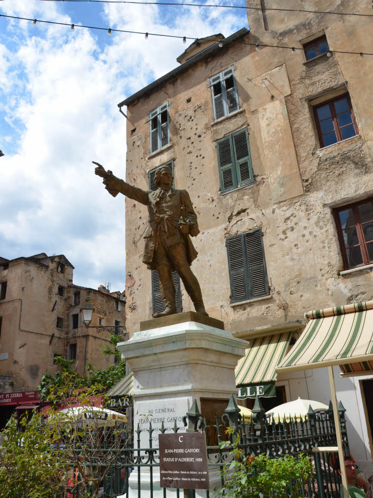 Corte: Denkmal von  Gianpietro Gaffori vor zerschossener Hausfassade. Gaffori organisierte  den Widerstand gegen die Besatzer aus Genua.