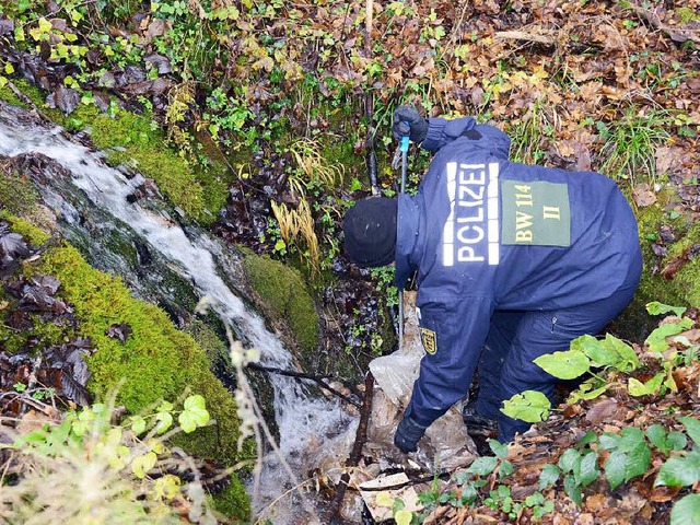 Ein Polizeibeamter durchsucht  ein Wal...ggeworfene Tte wird genau inspiziert.  | Foto: dpa