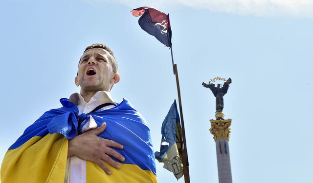 In die Landesflagge gehllt, singt ein...n Kiew die Nationalhymne der Ukraine.   | Foto: AFP