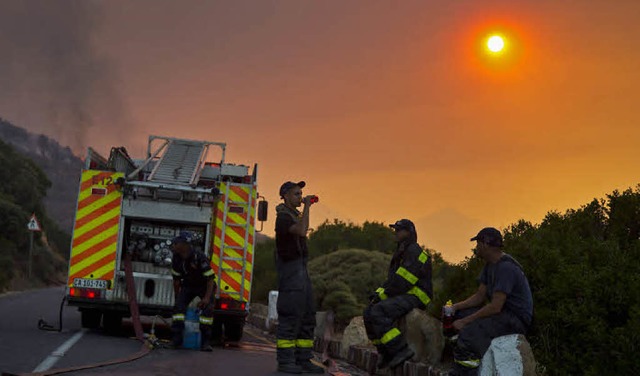 Feuerwehrmnner machen eine Pause vor der vom Rauch verdunkelten Sonne.  | Foto: dpa