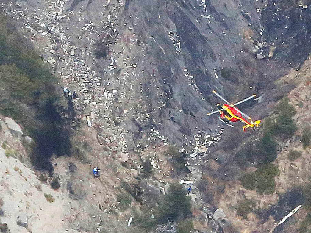 Ein Helikopter fliegt am 24.03.2015 ber eine Stelle an der Helfer neben Wrackteilen arbeiten,