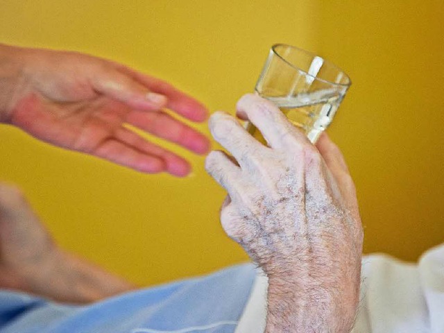 Eine Krankenpflegerin reicht einem Patienten ein Glas Wasser.  | Foto: dpa