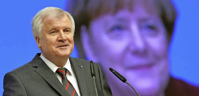 Mienenspiel: Seehofer  spricht im Deze...ei der Kanzlerin auf einer Leinwand.    | Foto: AFP