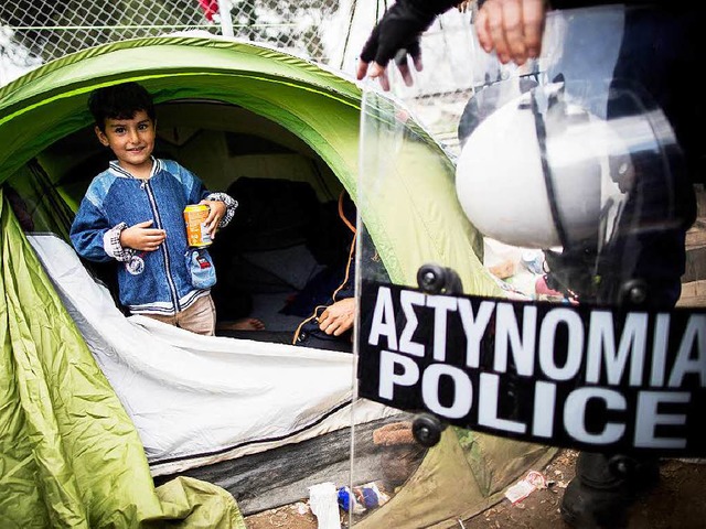Ein Flchtlingsjunge steht im Flchtli... Schild eines griechischen Polizisten.  | Foto: dpa