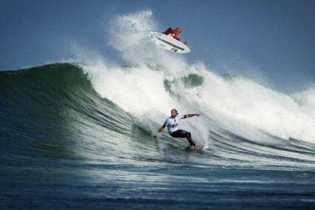 Kelly Slater springt und steht den ersten Seven-Twenty auf einem Surfbrett