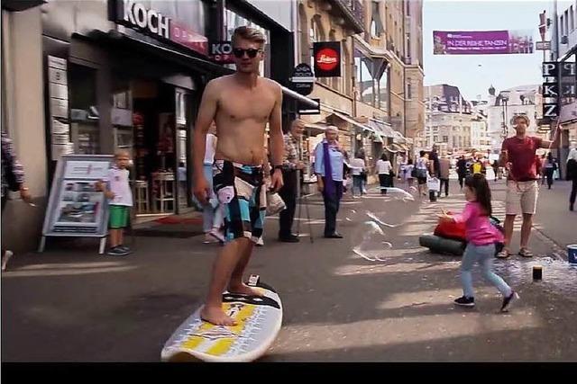 Typ ohne Hemd rollt mit Surfbrett durch Basler Innenstadt