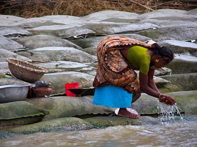 Eine Frau wscht sich am Ufer des Brahmaputra &#8211; und steht auf Sandscken.  | Foto: Germund
