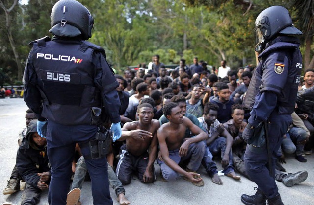 Migranten aus Schwarzafrika, von spanischen Polizisten bewacht   | Foto: DPA