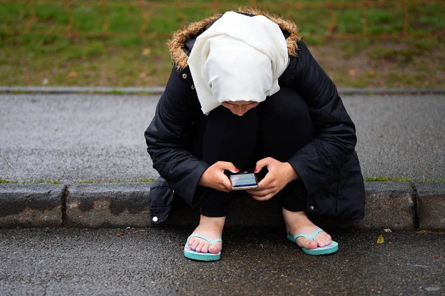 Eine Asylbewerberin sitzt vor einer  E...chtlinge mit ihrem Handy in der Hand.  | Foto: dpa