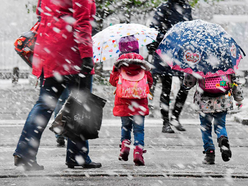 Zwei Kinder mit Regenschirmen gehen am Dienstag in Mnchen  bei Schneefall ber eine Strae.