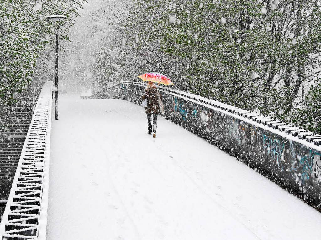 Eine Frau geht am Dienstag in Mnchen  bei Schneefall ber eine verschneite Fugngerbrcke.