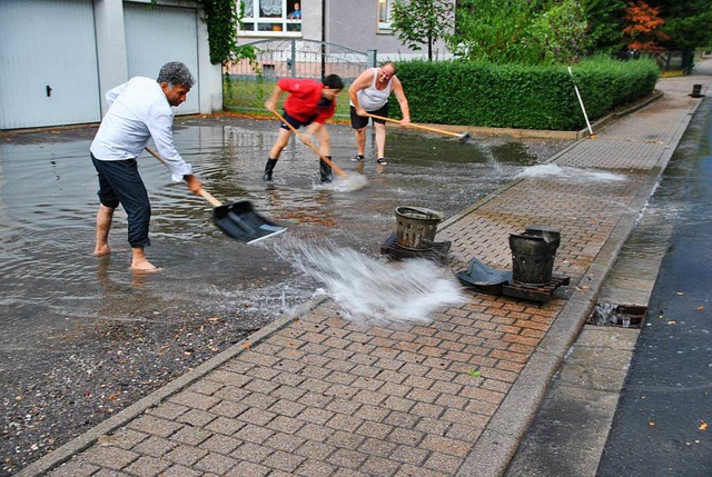 Anwohner schippen Wasser einer berflu...e in Btzingen zu den Ablaufschchten.  | Foto: Manfred Frietsch