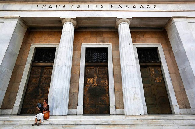 Eine Frau sitzt in Athen vor der Bank von Griechenland.  | Foto: dpa