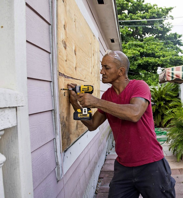 Ein Mann sichert die Fenster seines Hauses mit Holzplatten vor dem Sturm.  | Foto: AFP