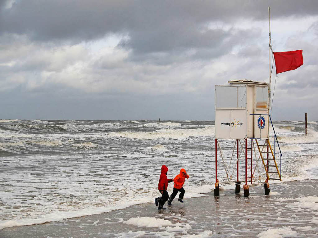 Kinder  auf dem Strand von Wangerooge (Niedersachsen) laufen bei strmischen Wind vor den Wellen davon.
