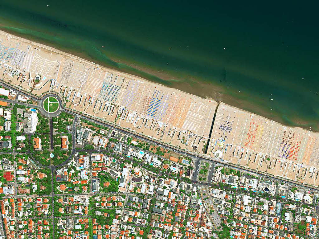 „Strandbewirtschaftung“: Militrisch exakt angeordnet und durch ihre Farbe gut unterscheidbar bedecken Sonnenschirme die Adriakste bei Rimini.