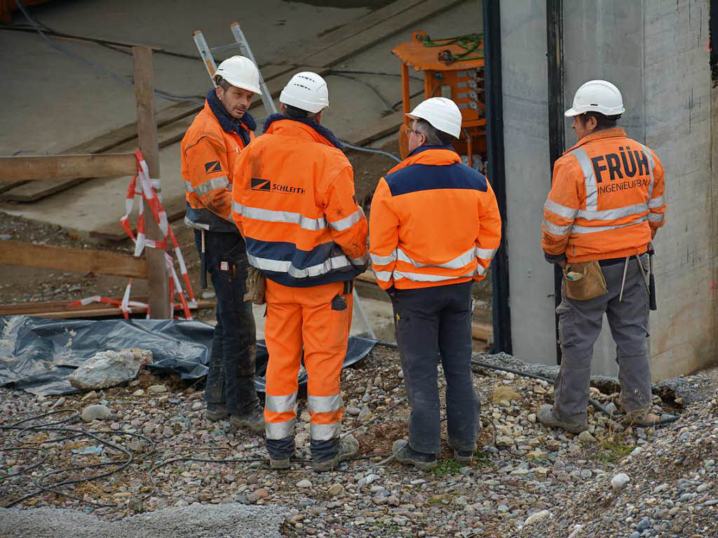 Beteiligte Bauarbeiter unterhalten sich vor dem Rahmenbauwerk.
